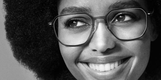 Black and white close-up of a smiling woman wearing Lindberg n.o.w. prescription glasses with a lightweight geometric frame.