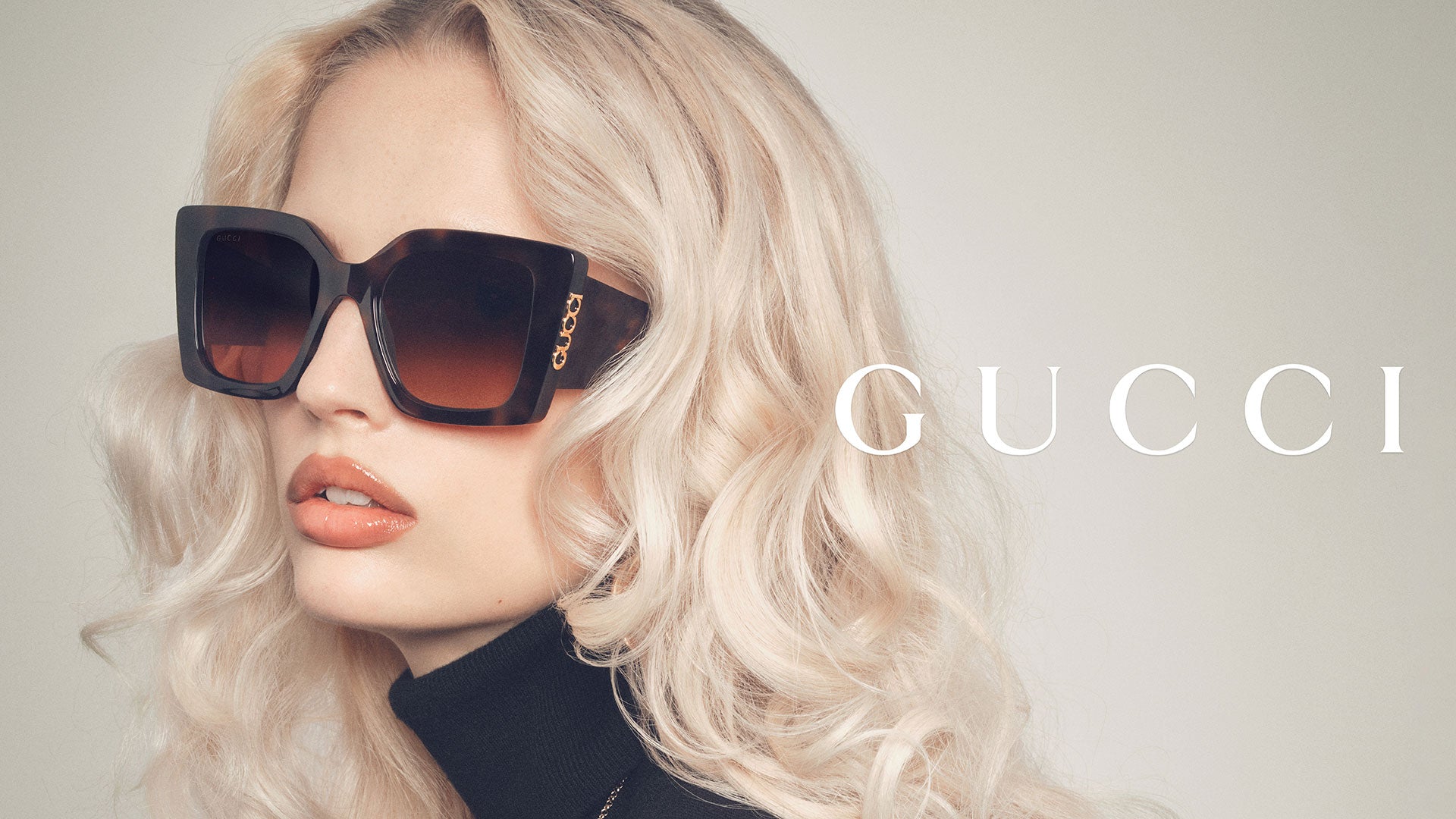 Close-up portrait of a woman wearing oversized Gucci sunglasses featuring a tortoiseshell frame and brown gradient lenses. The bold and sophisticated design enhances a glamorous look while reflecting the elegance and exclusivity of Gucci eyewear.