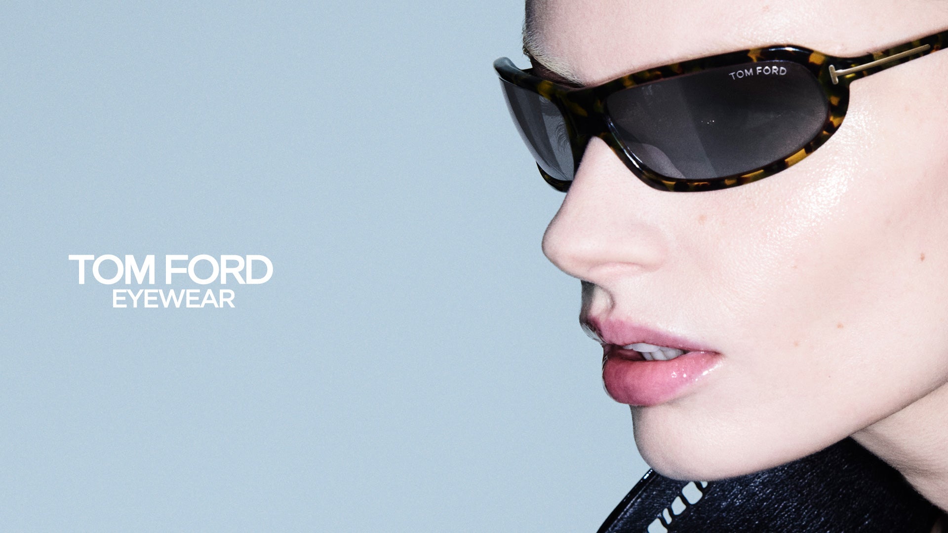 Close-up of a female model wearing Tom Ford FT1400 tortoiseshell sunglasses with dark lenses and Tom Ford Eyewear logo on a light blue background - giarre.com